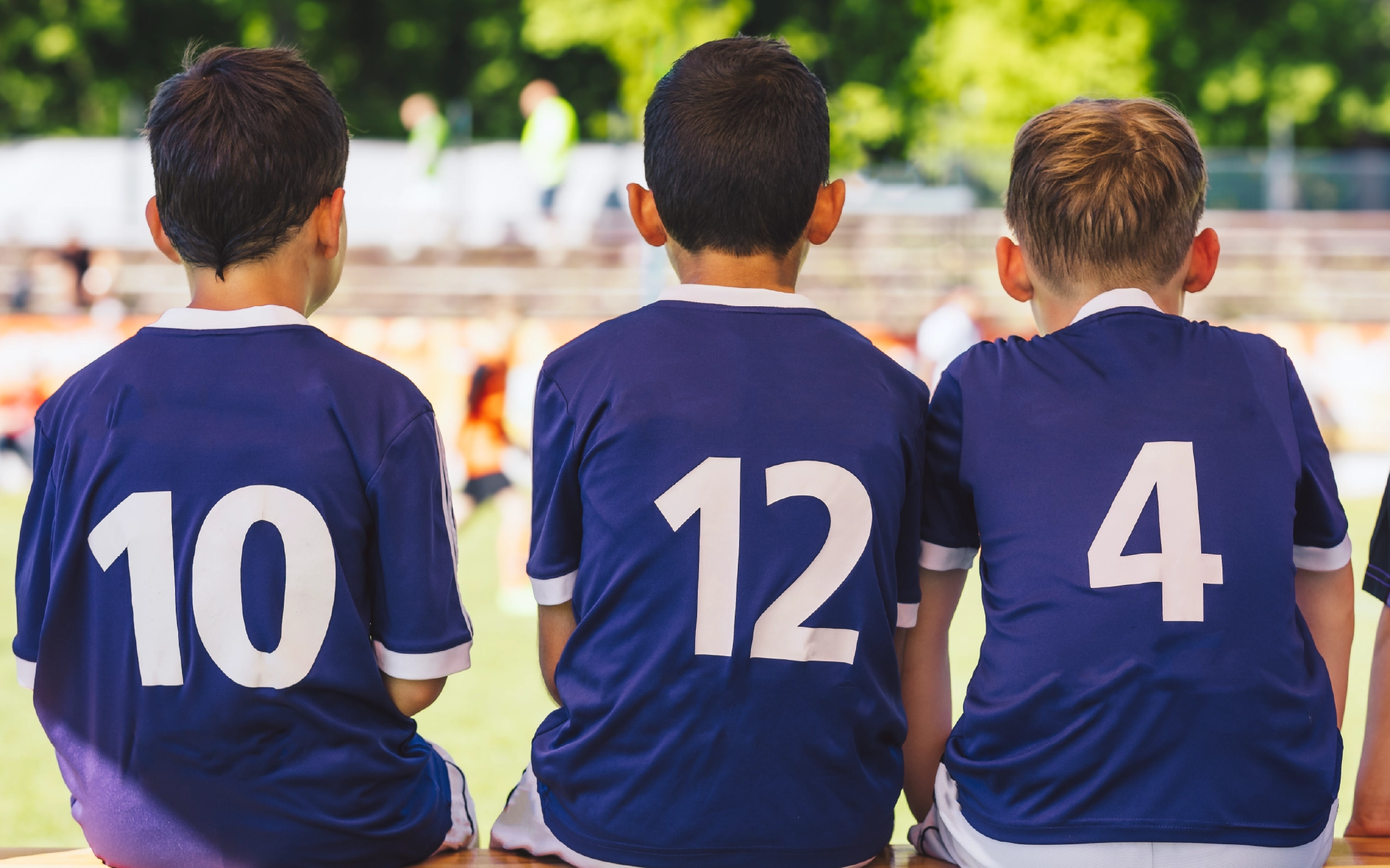 three young boys sitting on the team bench with custom made jerseys