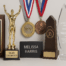 Engraved sports trophies and medals on a workshop bench next to a laser engraver at a custom shop in Austin