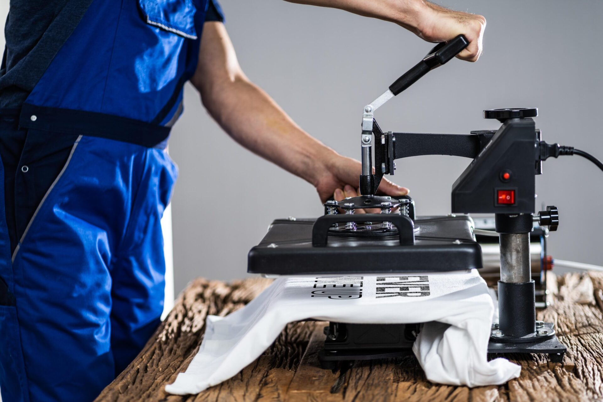 Print technician pressing down the handle of a heat press machine onto a custom printed white t-shirt, demonstrating the professional heat press printing process for custom apparel orders at The Logo Store in Austin TX