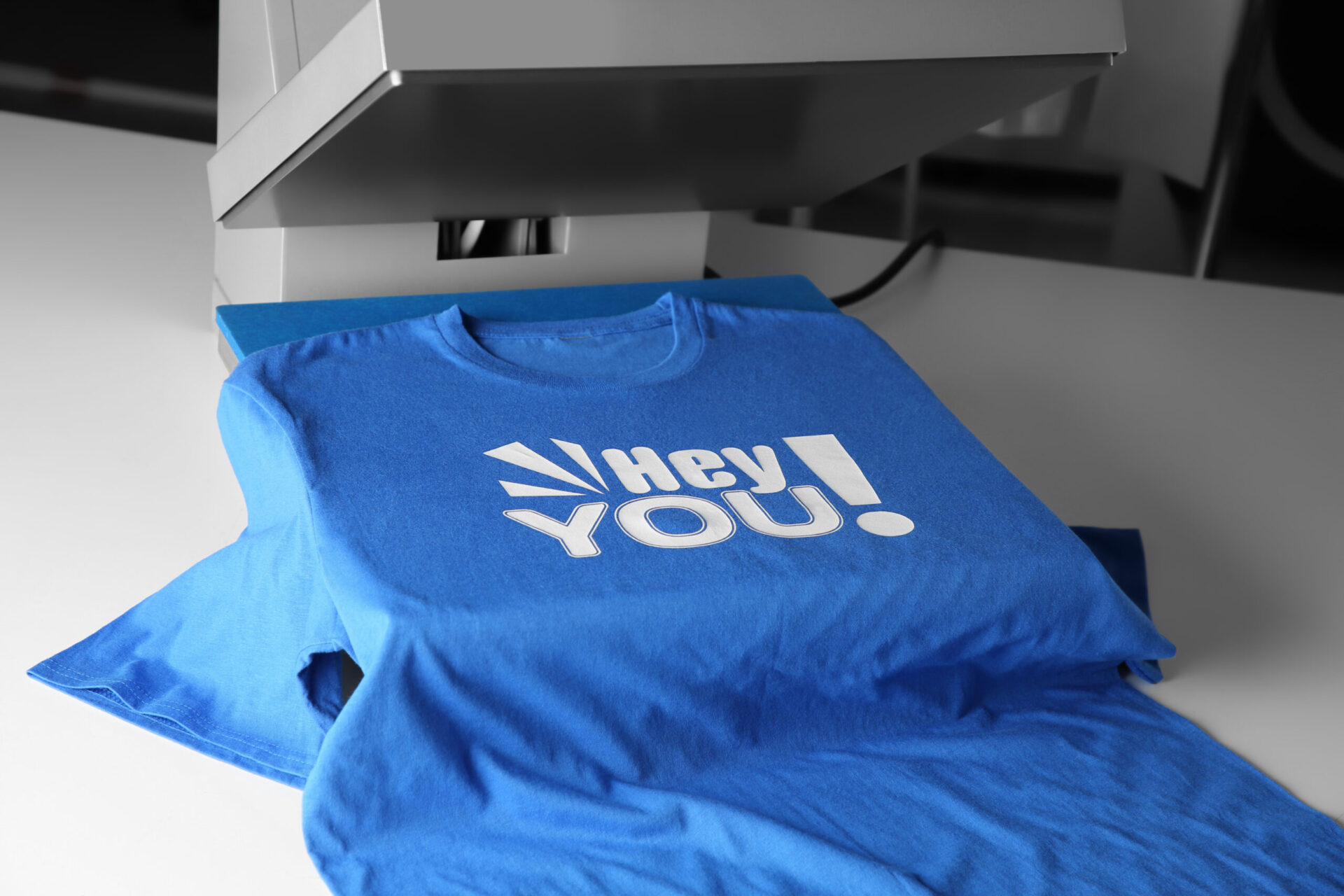 Finished custom heat press printed blue t-shirt displaying a bold white graphic design fresh off the heat press machine, showing the vibrant and sharp results of professional custom heat press printing services for branded apparel at The Logo Store in Austin TX