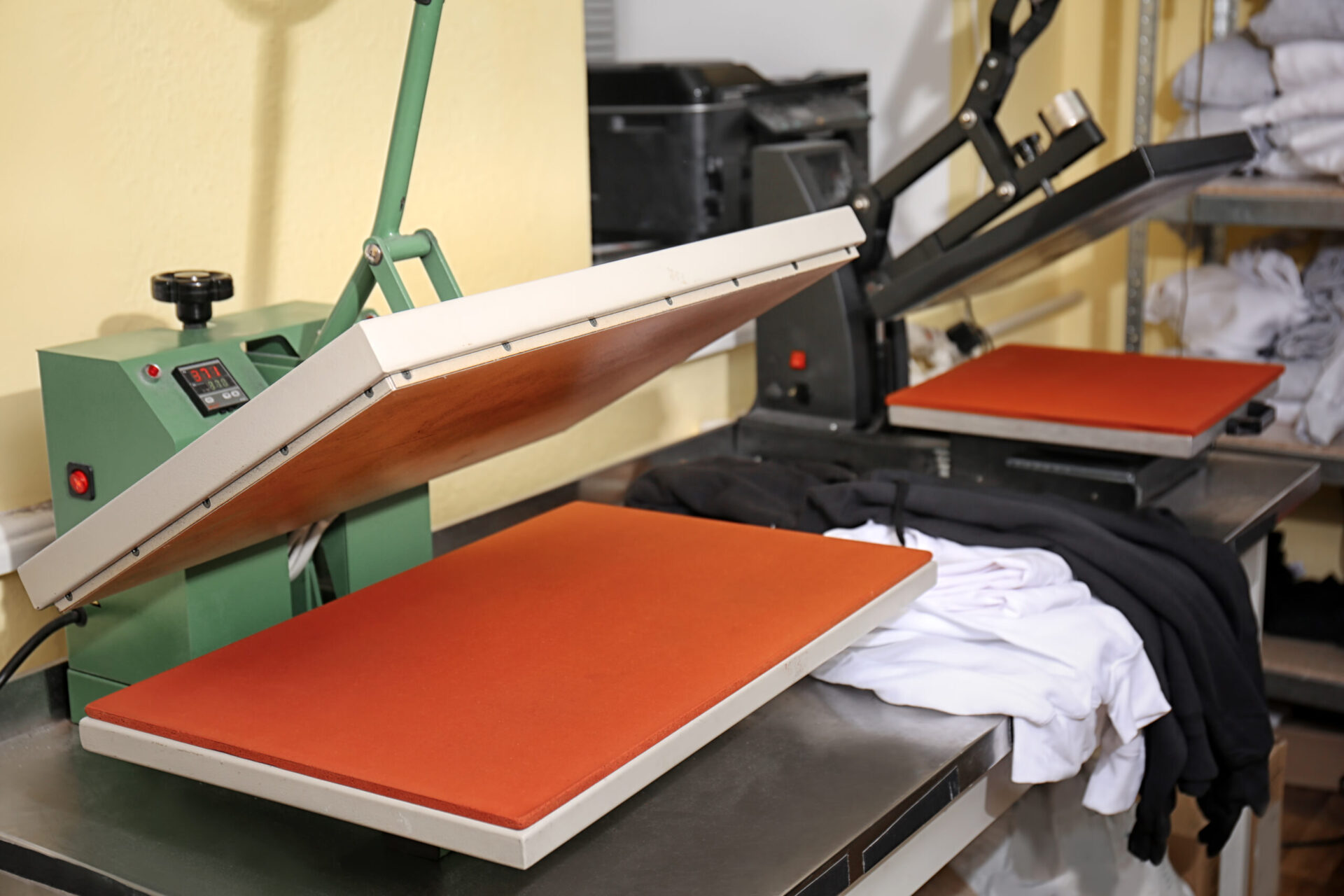 Professional heat press machine with platen raised open revealing a large silicone printing pad in a custom apparel print shop, showcasing the commercial heat press printing equipment used for custom branded t-shirt and apparel orders at The Logo Store in Austin TX