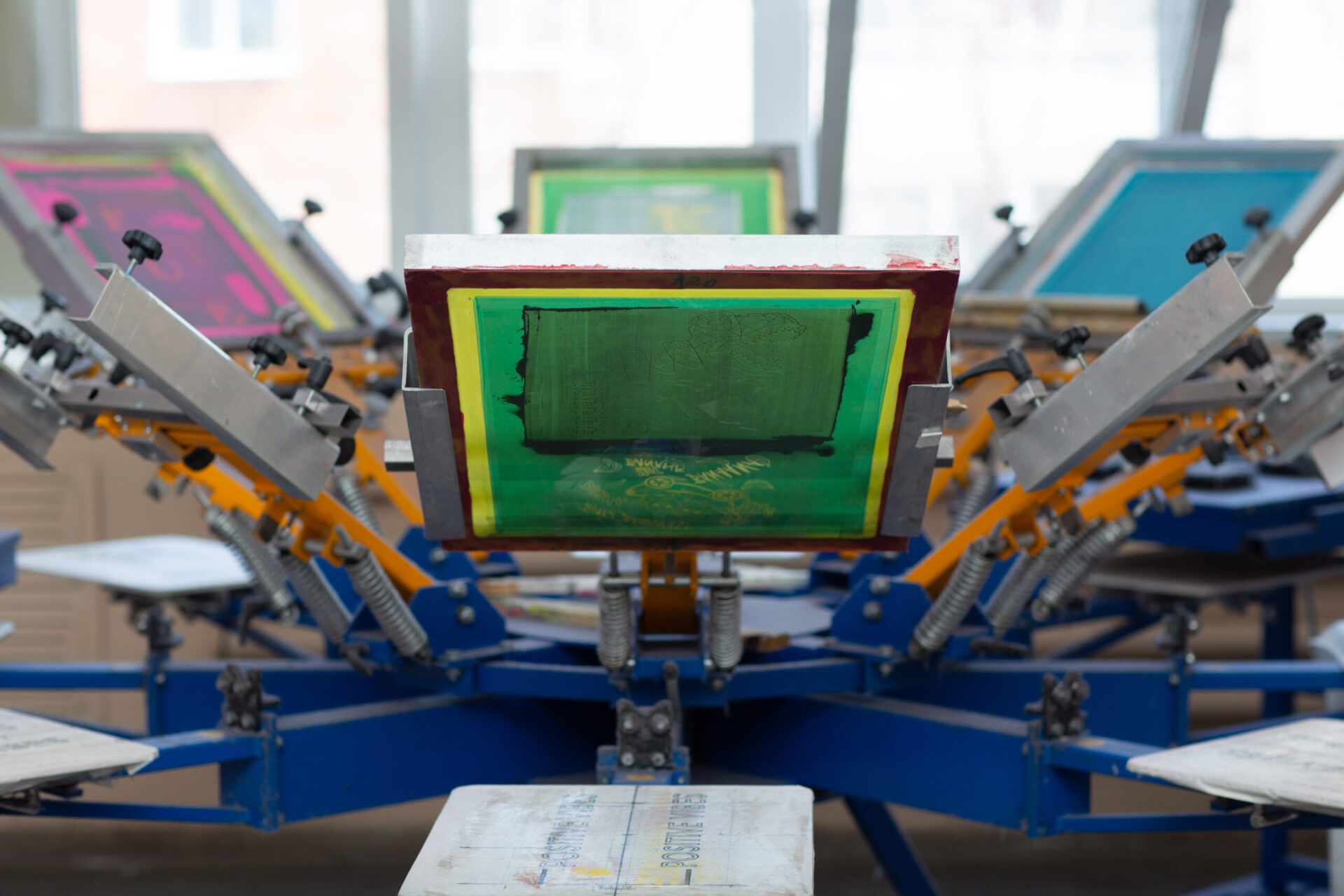 Multi-station screen printing carousel press loaded with colorful mesh screens ready for production, representing the professional custom shirt printing equipment used for no minimum orders at The Logo Store in Austin TX