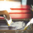 Screen printer applying white ink through a mesh screen with a squeegee on a professional multi-station press, showcasing the custom screen printing process available for businesses and teams at The Logo Store in Austin TX