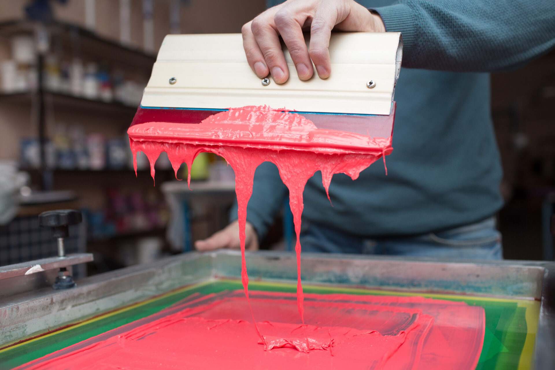 creen printer applying red ink through a mesh screen using a squeegee at a custom print shop, demonstrating the step-by-step screen printing process used for custom t-shirts and branded apparel in Austin and San Antonio