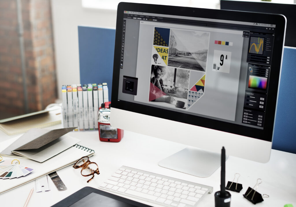 Graphic designer working at a desktop computer with Adobe Illustrator open, surrounded by color swatches and design tools, showing the professional software used to create and prepare a vector file for screen printing