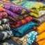 Stacks of folded custom t-shirts in red, teal, gray, and gold, ready for an Austin event order.