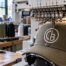 Multi-needle embroidery machine stitching a CB circle monogram onto an olive structured mesh-back trucker hat at a custom shop in Austin