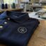 A polo with a generic monogram embroidered on the left chest next to a placement ruler at a custom embroidery shop in Austin