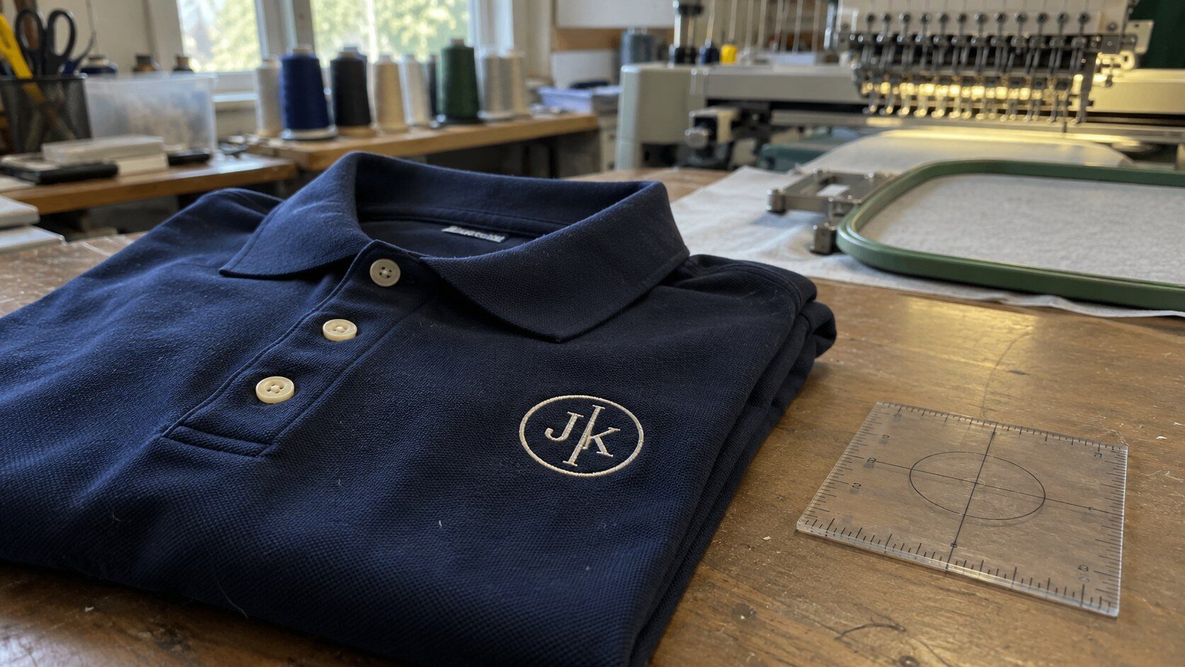 A polo with a generic monogram embroidered on the left chest next to a placement ruler at a custom embroidery shop in Austin